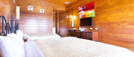 A wooden-paneled room with a large bed, a flat-screen TV mounted on the wall, and a wooden dresser.