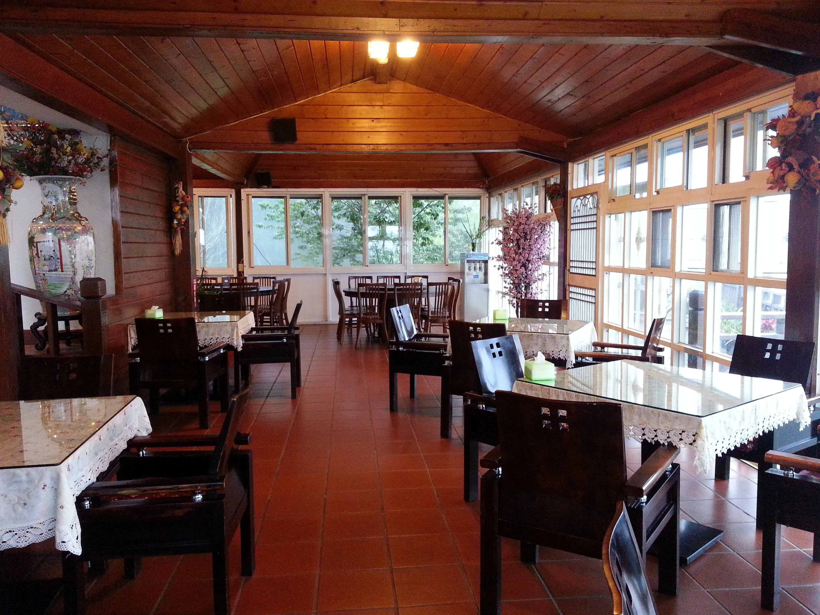 A restaurant with wooden interior, tiled floor, and large windows. Tables and chairs are arranged for dining.