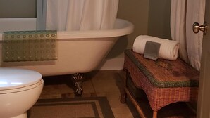 Ein Badezimmer mit einer weißen Badewanne, einer Toilette und einem Korbstuhl.