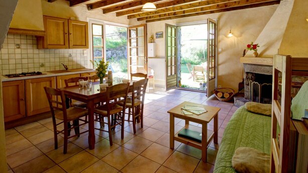 A cozy kitchen with wooden cabinets, a dining table, and chairs. There is a fireplace and a small table with a vase of flowers. - Authentic cottage with fireplace, pets allowed and WiFi by the forest (La Versanne)
