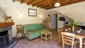 A cozy living room with a green sofa, a fireplace, a dining table with chairs, and a kitchen area with a microwave and stove. - Authentic cottage with fireplace, pets allowed and WiFi by the forest (La Versanne)
