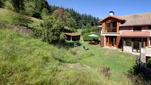 A two-story wooden house with a stone foundation, surrounded by a grassy yard and dense forest. - Authentic cottage with fireplace, pets allowed and WiFi by the forest (La Versanne)