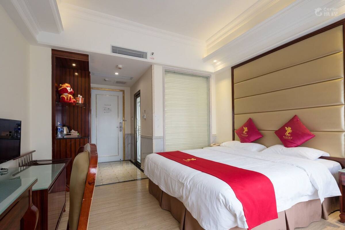 A hotel room with a bed, a desk, a chair, a television, a wardrobe, and a door leading to another room.