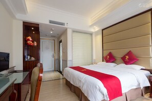Habitación de hotel con cama, escritorio, silla, televisor, armario y puerta que da a otra habitación.