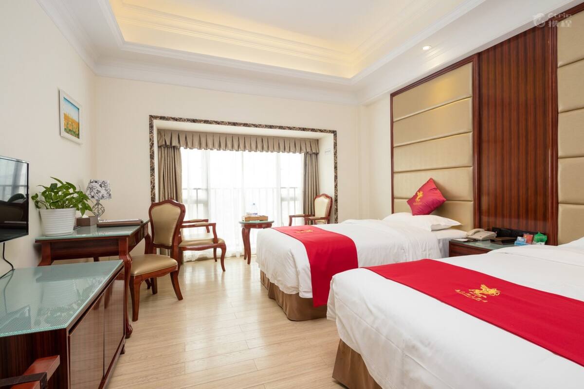 A hotel room with two beds, a desk, a chair, a TV, and a window with curtains.