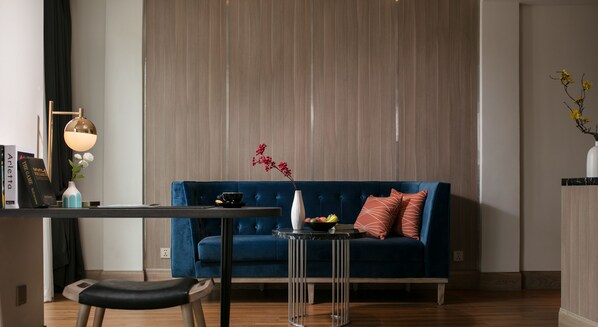 A modern living room with a blue sofa, a small side table with a vase and fruit bowl, a black chair, and a lamp.