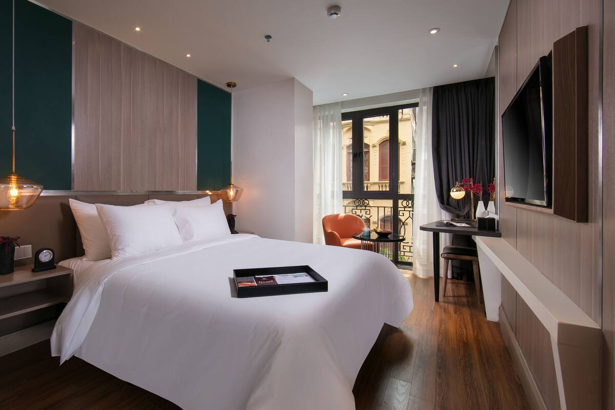 A modern hotel room with a large bed, bedside table, and a TV mounted on the wall.