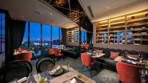 A restaurant with a city view, seating arrangements, and a wine rack. - Aurora Premium - A Lifestyle Hotel (Hanoi)