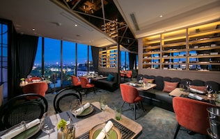 A restaurant with a city view, seating arrangements, and a wine rack.