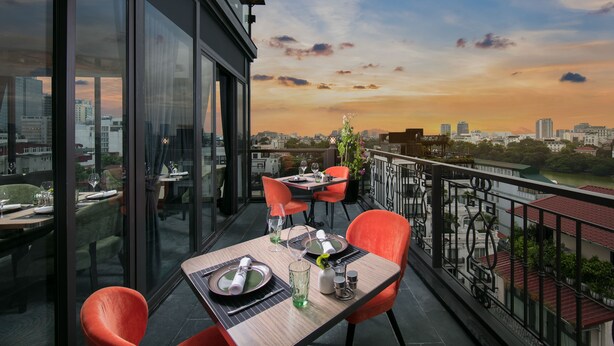 A dining area with a table set for two, overlooking a cityscape at sunset. - Aurora Premium - A Lifestyle Hotel (Hanoi)
