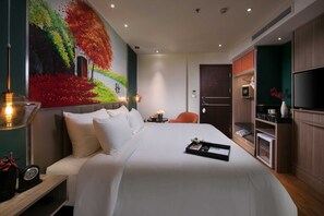 A hotel room with a large bed, a painting on the wall, a TV, and a minibar. - Aurora Premium - A Lifestyle Hotel (Hanoi)