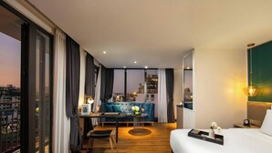 A modern hotel room with a large bed, a desk with a chair, a sofa, and a view of the cityscape. - Aurora Premium - A Lifestyle Hotel (Hanoi)