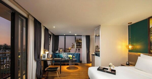 A modern hotel room with a large bed, a desk with a chair, a sofa, and a view of the cityscape. - Aurora Premium - A Lifestyle Hotel (Hanoi)