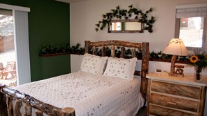 Un dormitorio con estructura de cama de madera, colcha blanca acolchada, mesita de noche con lámpara y espejo sobre la cama.