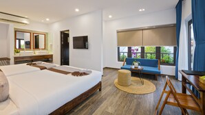 A modern hotel room with a large bed, a sofa, a dining table, a TV, and a bathroom with a mirror and sink. - December Hoi An Villa (Da Nang)