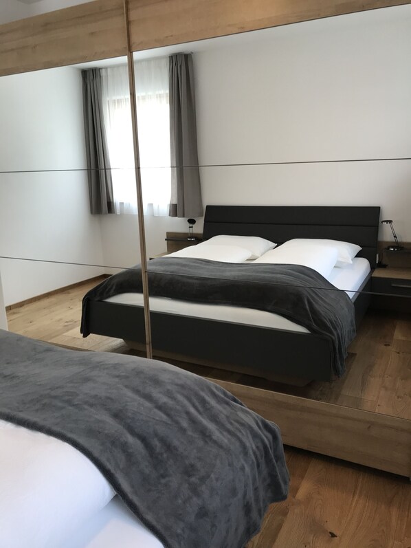 Ein modernes Schlafzimmer mit zwei Betten, Holzboden und einem großen Spiegel.