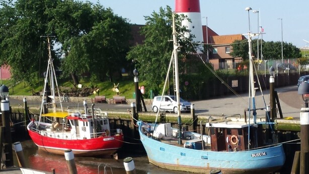 Et fyrtårn, en rød og hvid båd i lysthavnen, og en blå båd med navnet 'BUSUM'.