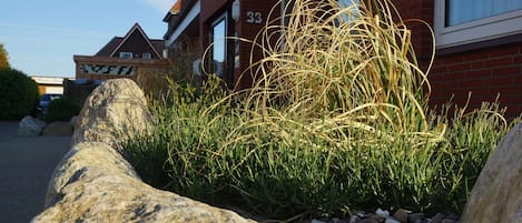 A residential building with a brick facade, numbered 33, and a garden area with tall grasses and rocks.