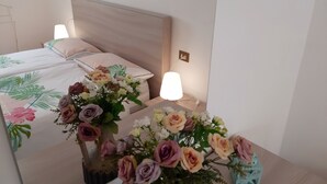 A neatly made bed with floral bedding, a bedside table with a vase of flowers, and a wall-mounted lamp.