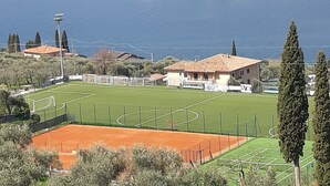 A sports field with a soccer goal, a tennis court, and a building with a tiled roof.