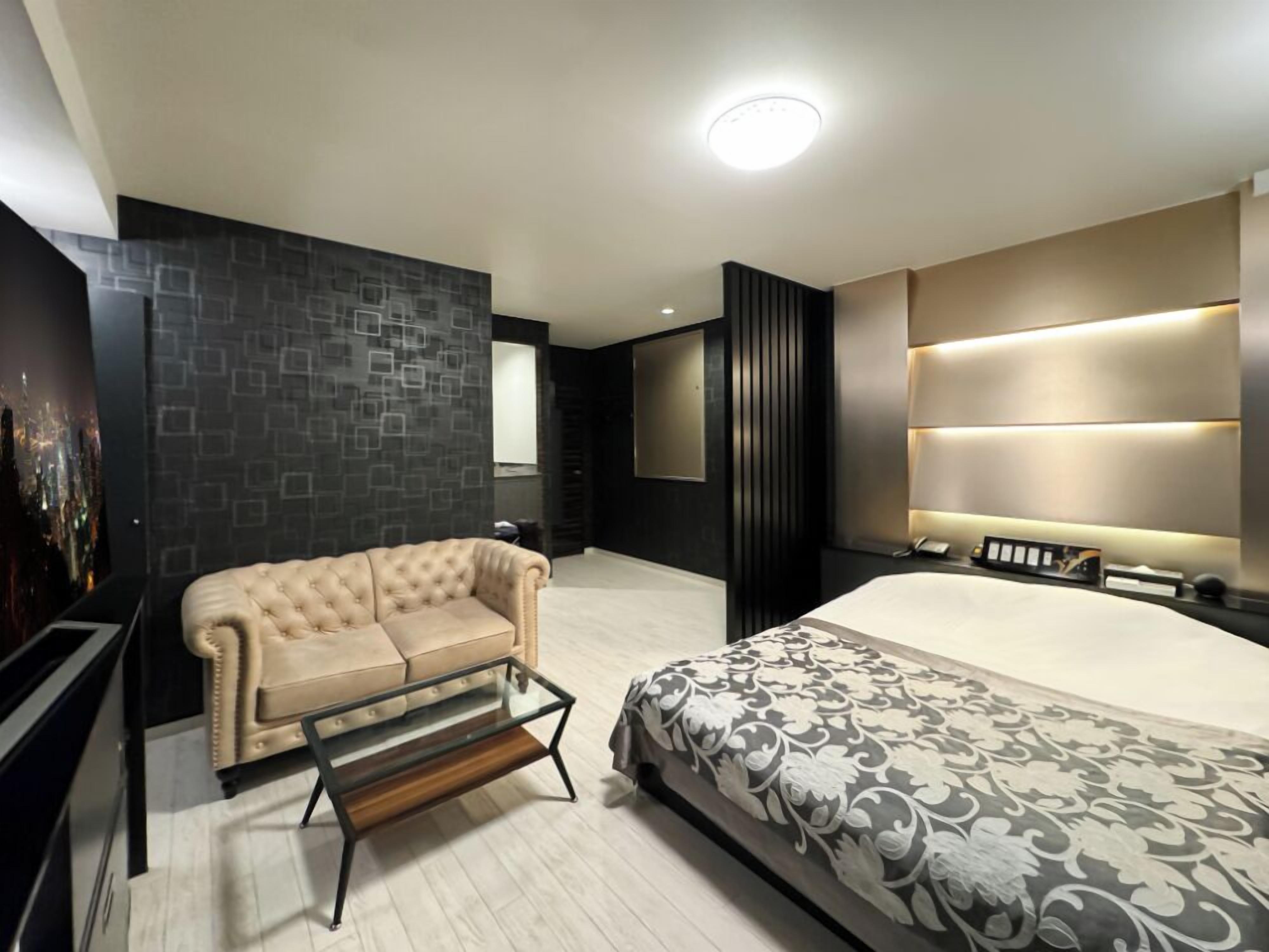 Una habitación de hotel moderna con una cama, un sofá, una mesa de centro de vidrio y un cartel con vistas a la ciudad en la pared.