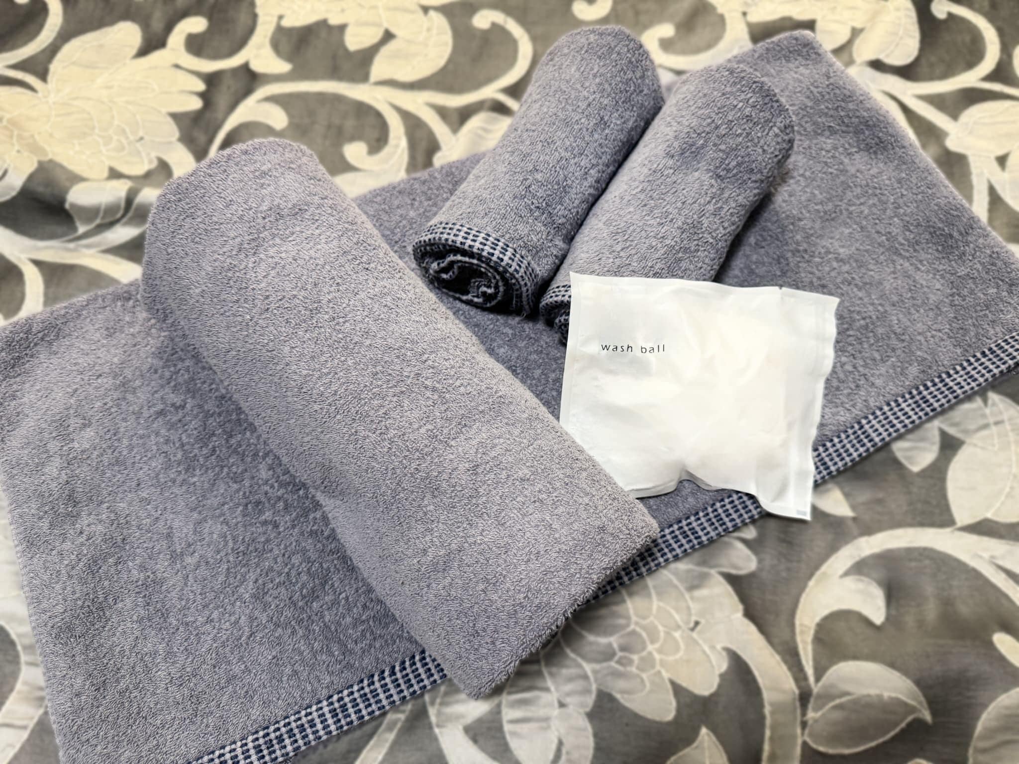 A neatly folded grey towel with a tag labeled 'wash ball' on a patterned fabric background.