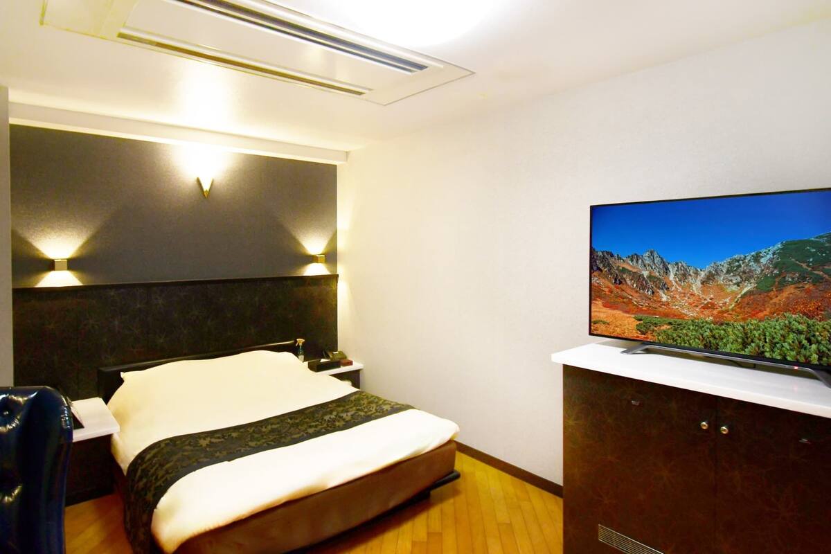 Una habitación de hotel con una cama, un televisor en un mueble y una lámpara fijada a la pared.