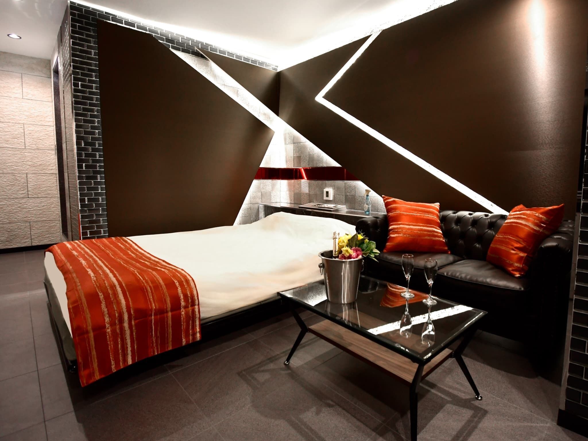 A modern hotel room with a bed, a glass coffee table, a sofa, and a fireplace.