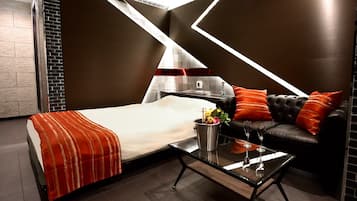 A modern hotel room with a bed, a glass coffee table, a sofa, and a fireplace.