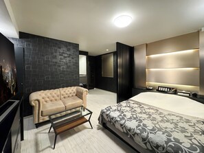 Une chambre d’hôtel moderne avec un grand lit, un canapé, une table basse en verre et une œuvre d’art murale représentant un paysage urbain.