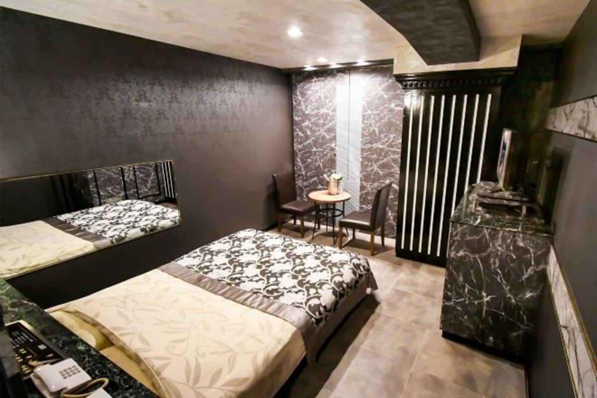 A hotel room with two beds, a desk, a chair, and a small table.