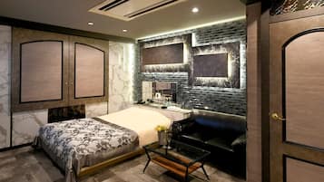 Un dormitorio moderno con cama, tocador con espejo, sofá de cuero negro y una mesa de centro de vidrio.