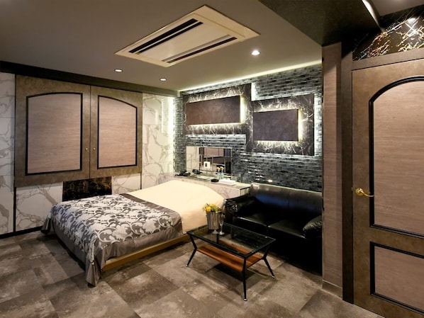Une chambre à coucher moderne avec un lit, une coiffeuse avec un miroir, un canapé en cuir noir et une table basse en verre.