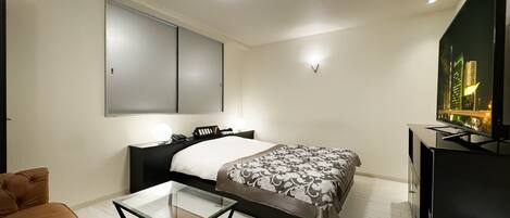 Una habitación de hotel moderna con una cama, una mesa de centro de vidrio, un sofá, un televisor y vistas a la ciudad.