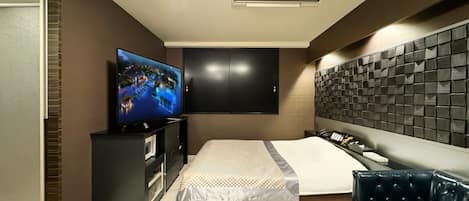 A modern hotel room with a large bed, a TV mounted on the wall, a dark-colored headboard, and a leather sofa.