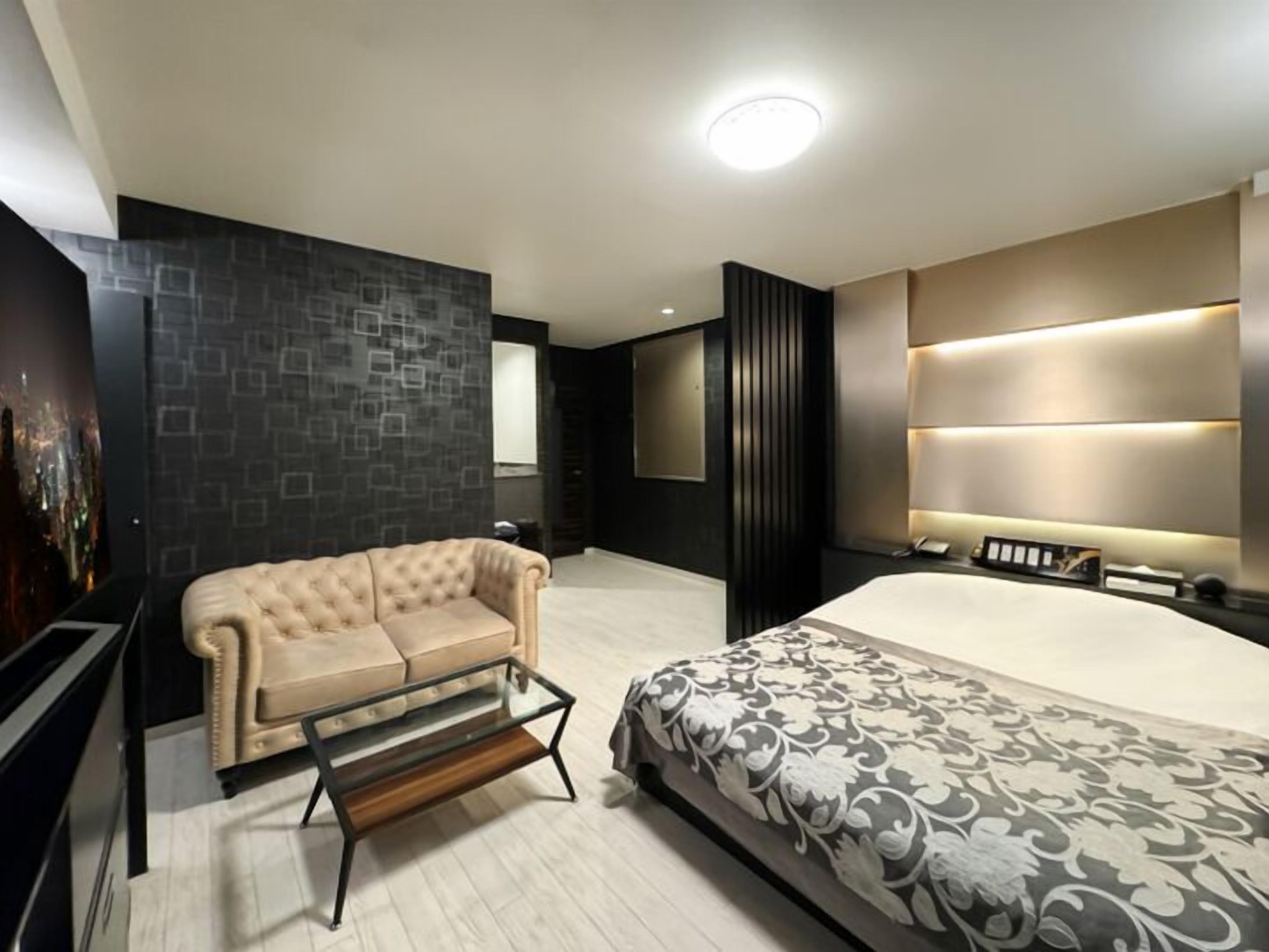 Un dormitorio moderno con una cama, un sofá, una mesa de centro de vidrio y una pared oscura con estampado.