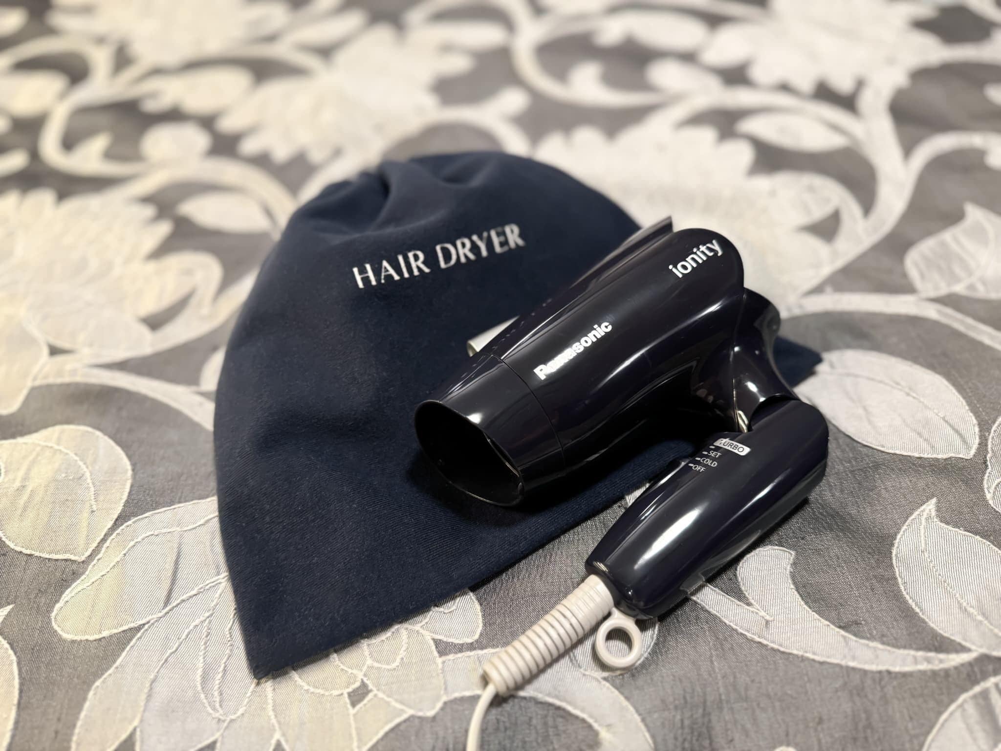 Un secador de pelo y una gorra con el texto 'HAIR DRYER' e 'ionity' sobre un fondo de tela estampada.
