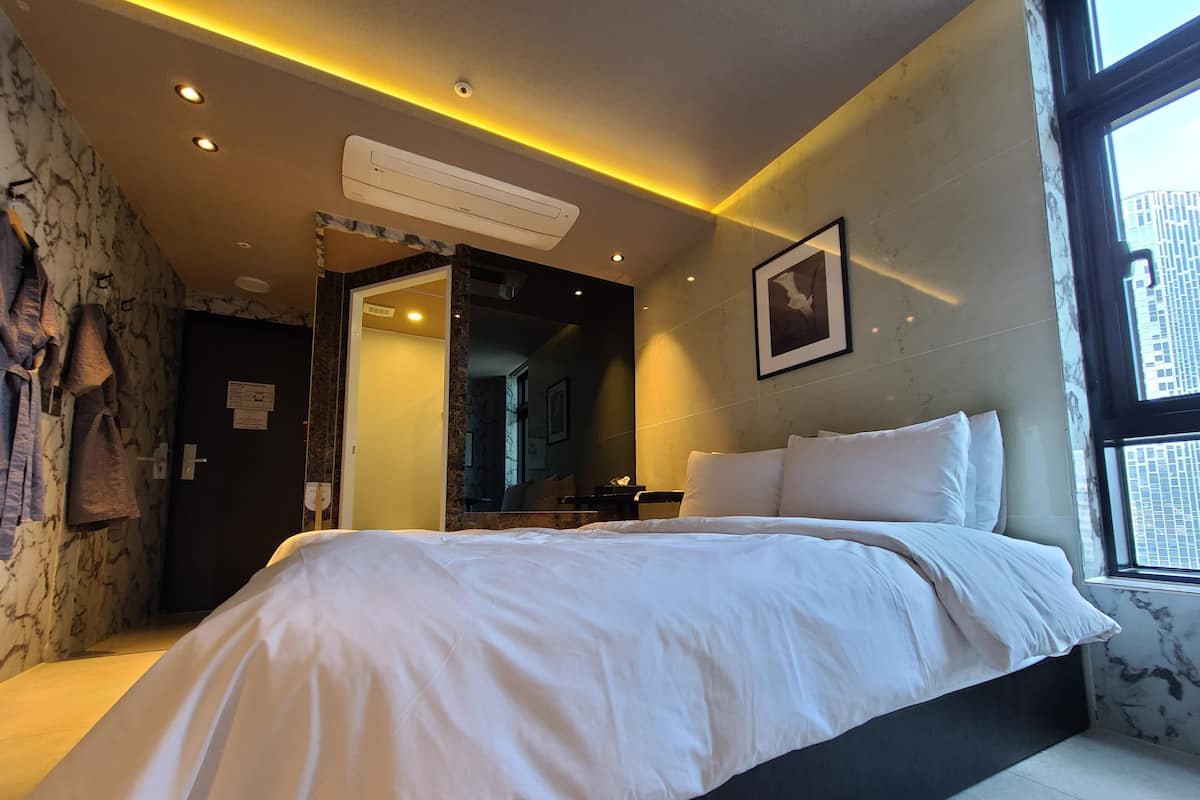 Habitación de hotel moderna con una cama grande, un espejo y una ventana con vista a la ciudad.