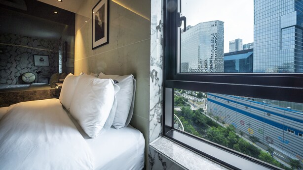 A hotel room with a bed, a marble wall, a framed picture, and a window with a city view. - MG Hotel Jonggak (Seoul)