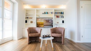 Una sala de estar moderna con dos sillones marrones, una mesa de centro blanca y una estantería llena de libros y objetos decorativos.