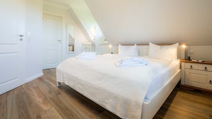 Un dormitorio con una cama grande, ropa de cama blanca, una mesita de noche y un espejo.