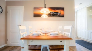 Comedor con una mesa de madera dispuesta para cuatro comensales, sillas blancas y una lámpara colgante.