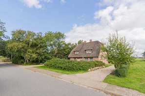 Une maison au toit de chaume, entourée d’une végétation luxuriante et dotée d’une allée pavée.