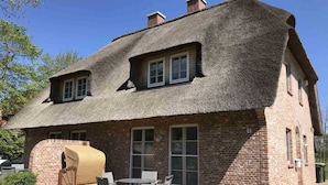 Una casa de ladrillo con tejado de paja, un patio con muebles de exterior y una chimenea de ladrillo.