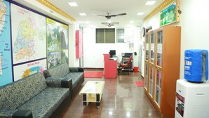 A reception area with a sofa, a small table, a map on the wall, a ceiling fan, and a water dispenser.