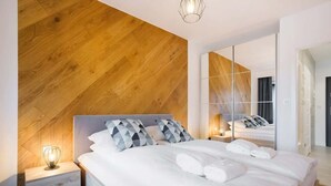 Una habitación de hotel moderna con una pared decorativa de madera, una cama grande con ropa blanca, una mesita de noche con una lámpara y un espejo de cuerpo entero.