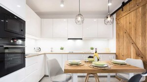 Una cocina moderna con armarios blancos, una mesa de comedor de madera e iluminación colgante.