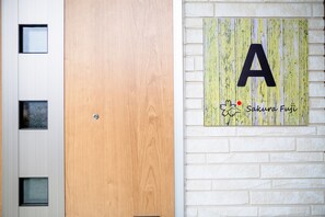 Une porte en bois, adossée à un mur sur lequel figure une grande lettre « A » et le nom « Sakura Fuji ».