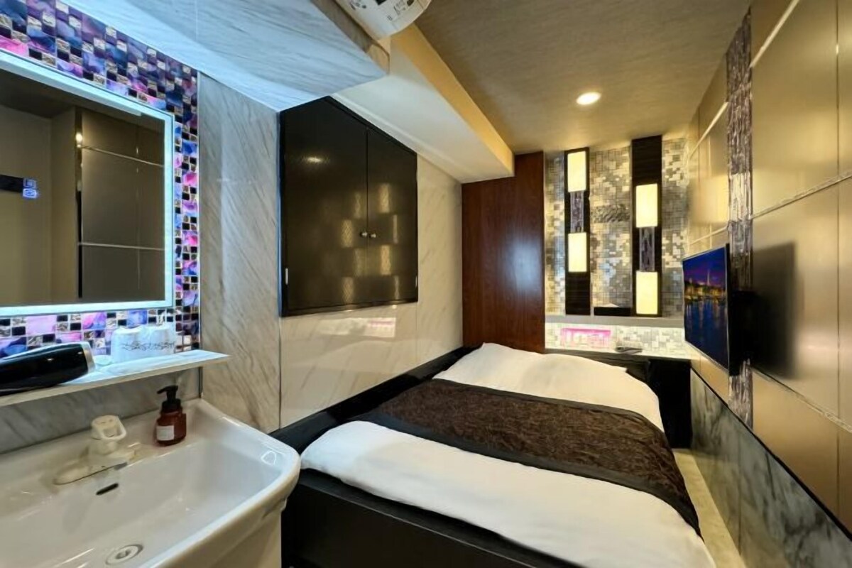 Una habitación de hotel moderna con una cama grande, un baño con lavamanos y espejo, y un televisor montado en la pared.
