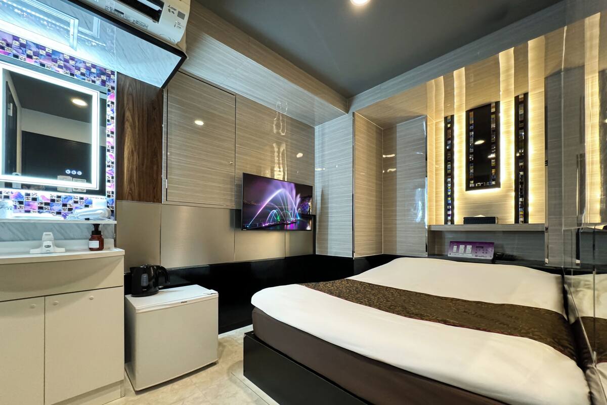 A modern hotel room with a large bed, a TV mounted on the wall, a bedside table, and a built-in wardrobe.
